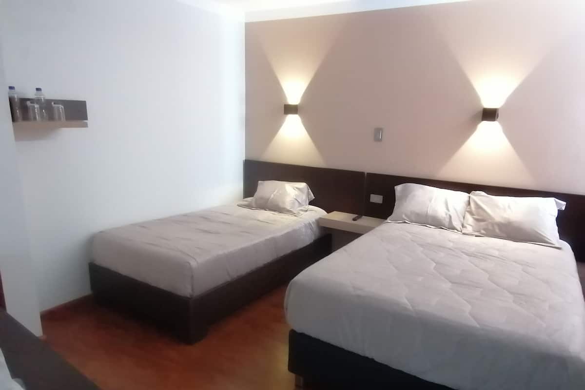 A hotel room with two beds, a nightstand, and a wall-mounted light fixture.