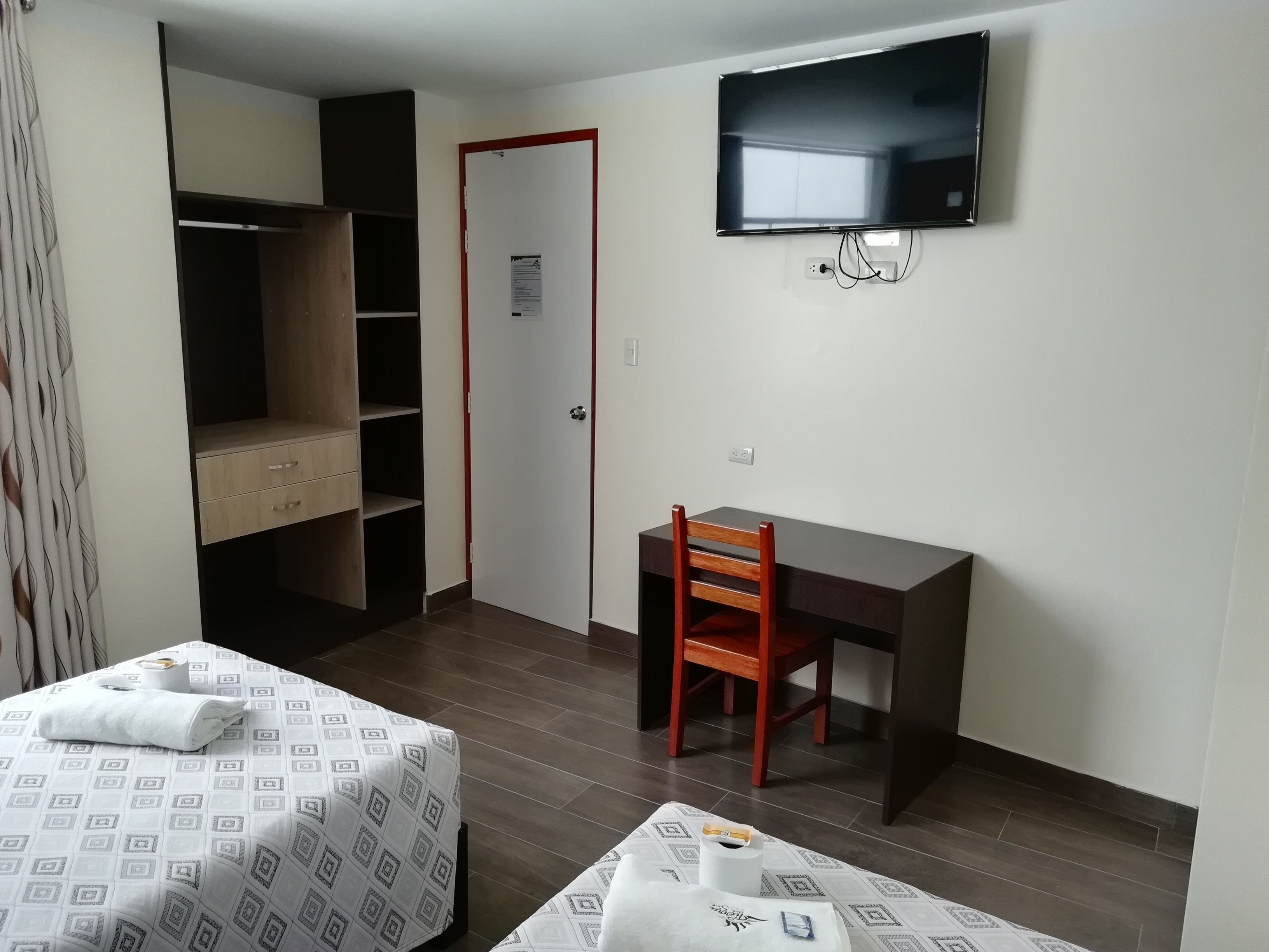 Habitación de hotel con cama, escritorio, silla, televisor y armario.