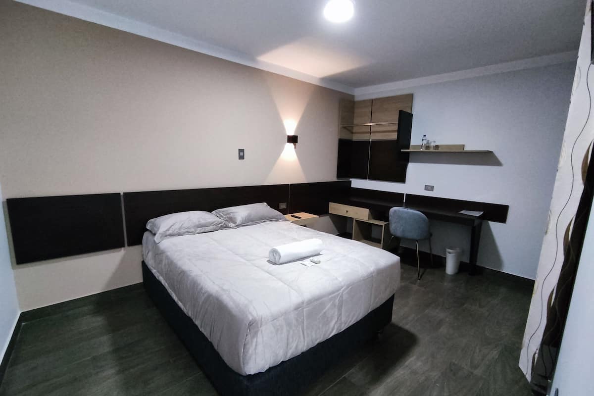 A hotel room with a bed, bedside table, chair, desk, and a mirror.
