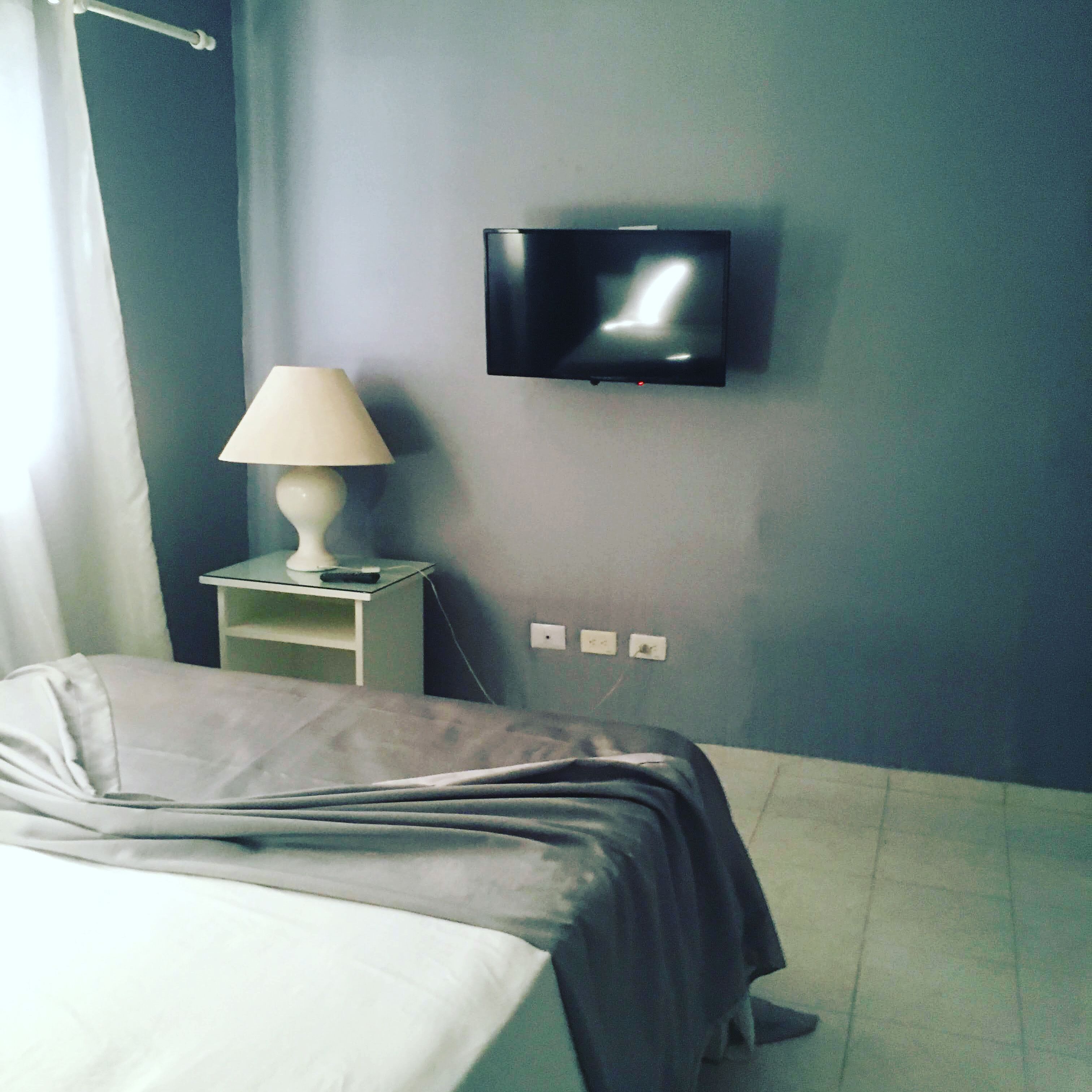 A bedroom with a bed, a nightstand with a lamp, and a wall-mounted TV.