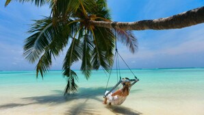 Escena de playa con una hamaca atada a una palmera, agua turquesa cristalina y cielo despejado.