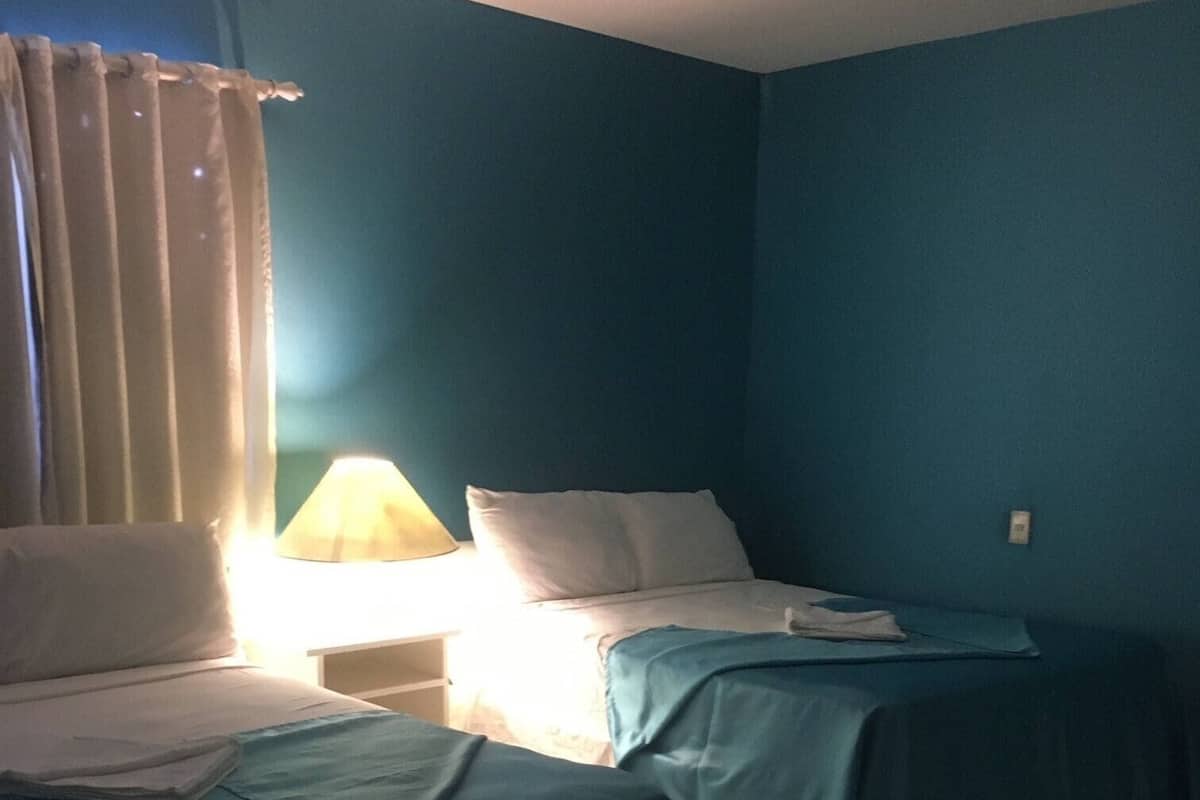 Una habitación con dos camas, una mesita de noche con lámpara y una cortina.