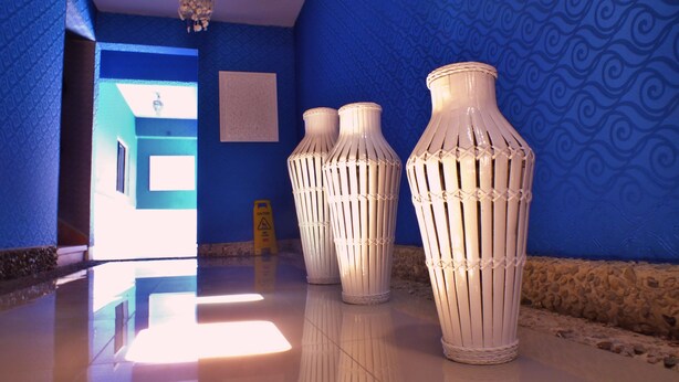 Un pasillo con paredes azuladas de diseño, tres jarrones blancos grandes y un letrero de precaución.