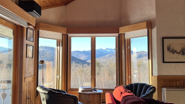 A cozy living room with a wooden ceiling, large windows offering a mountain view, a red sofa, and a black armchair. - Stunning views of Mt Washington and the presidentials. (Bartlett)
