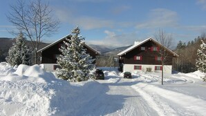 A snow-covered landscape with two wooden cabins, a dirt road, and parked cars. - Stunning views of Mt Washington and the presidentials. (Bartlett)