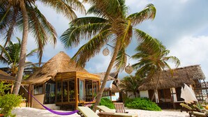 A beach resort with thatched-roof huts, palm trees, and sun loungers on the sand. - Casa Violeta (Tulum)