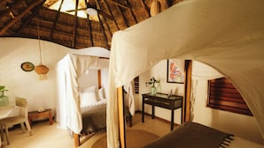 A room with a thatched roof, a bed with a canopy, a small table with a vase, and a chair. - Casa Violeta (Tulum)