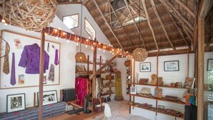 A boutique hotel interior with a rustic thatched roof, wooden shelves displaying various items, and a seating area with a patterned rug. - Casa Violeta (Tulum)