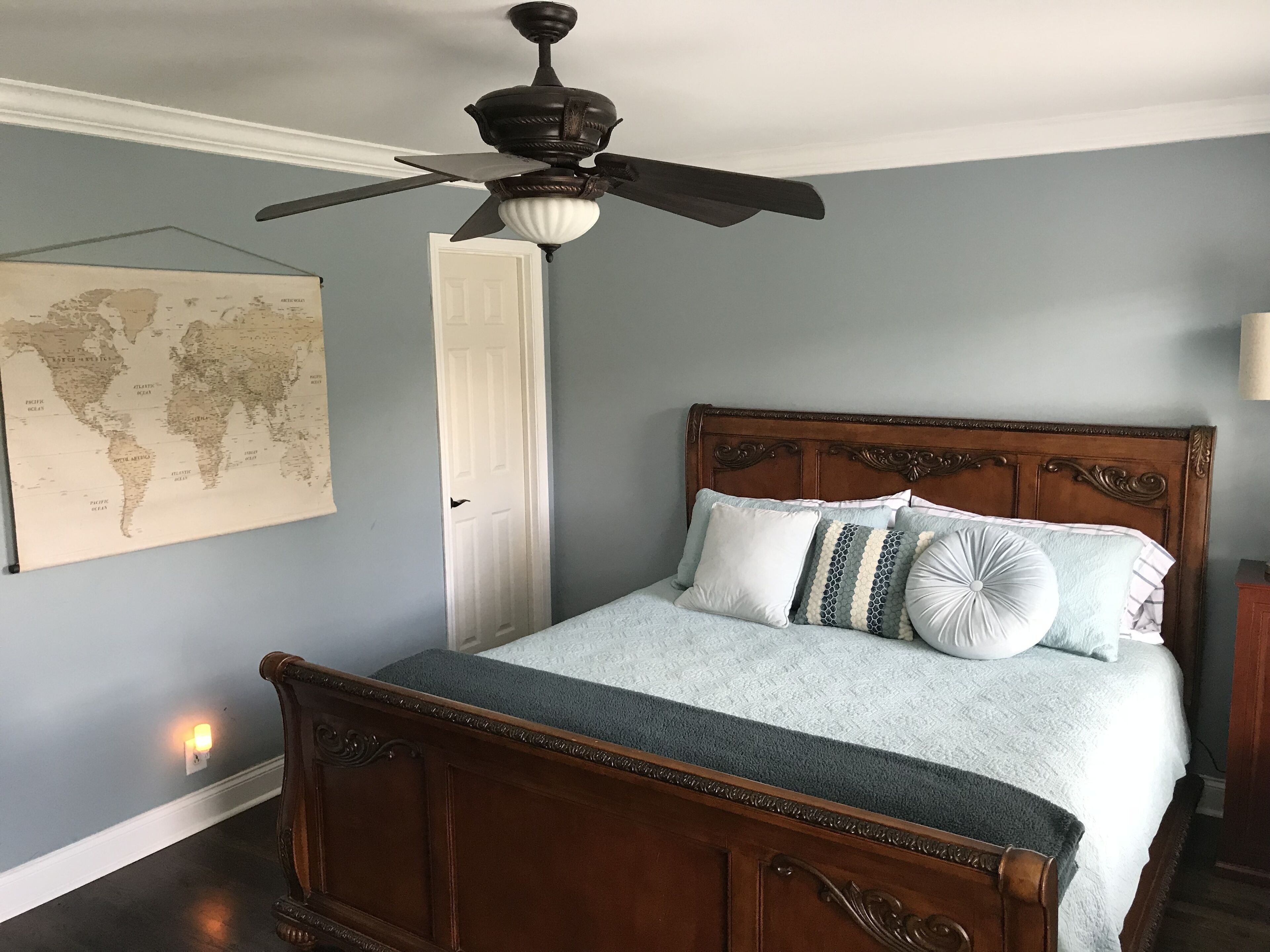 Ein Schlafzimmer mit einem hölzernen Bett, einer Weltkarte an der Wand und einem Deckenventilator.