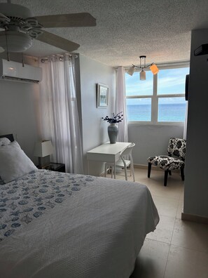 Une chambre à coucher comprenant un lit, un bureau, une chaise, une fenêtre donnant sur la mer et un ventilateur de plafond.
