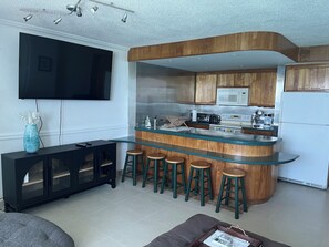 Una cocina moderna con una isla curva, taburetes de bar, un televisor de pantalla plana y armarios de madera.