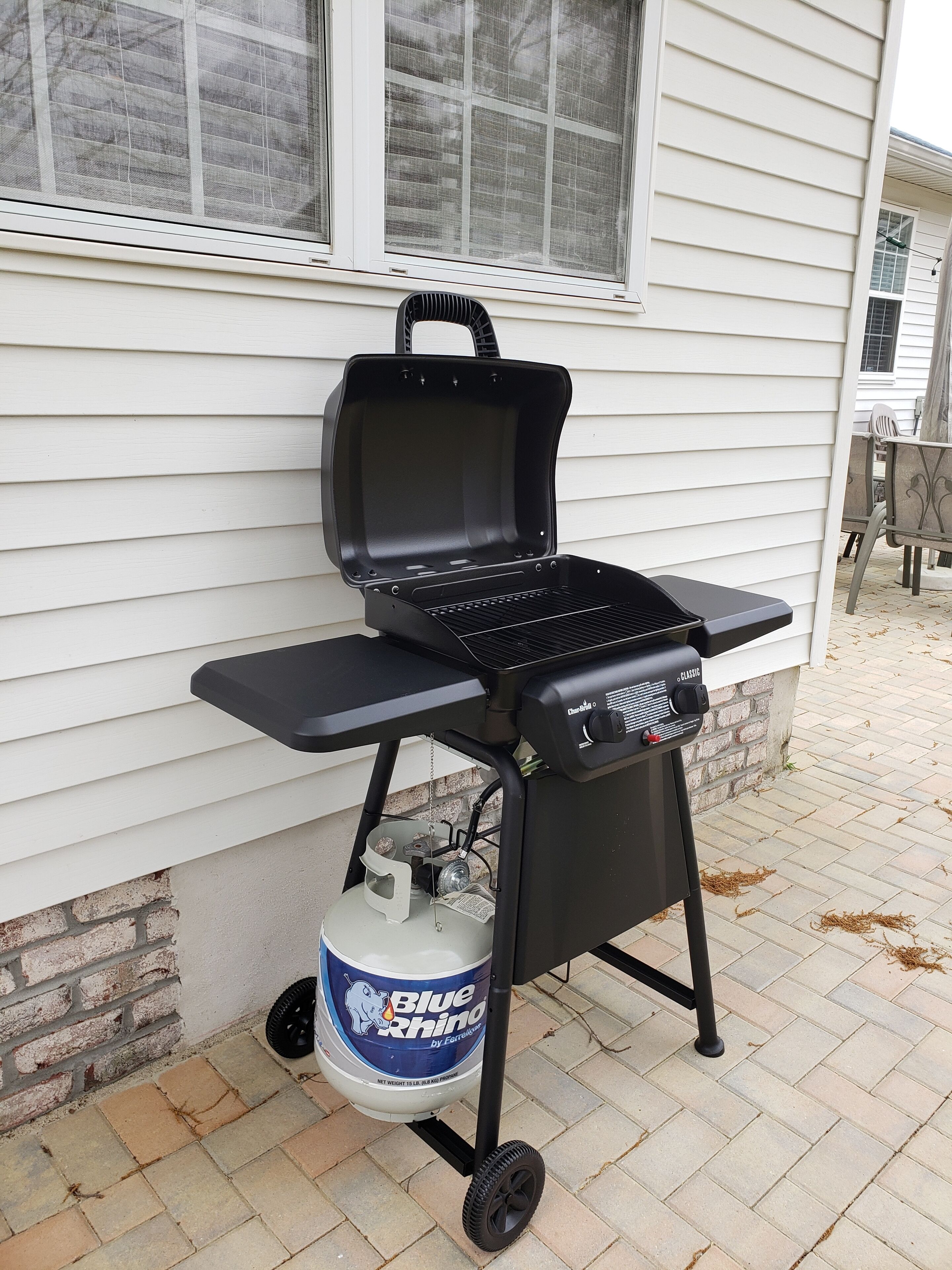 Un barbecue portatif avec une bouteille de propane, placé sur une terrasse en briques.