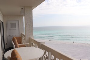 A balcony with a view of the beach, a door, and a table with chairs.