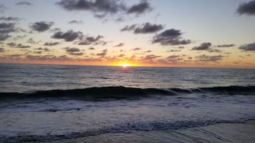 A sunset over the ocean with waves approaching the shore.