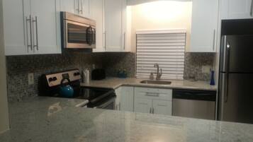 A kitchen with white cabinets, a stainless steel refrigerator, a microwave, a stove, and a sink.