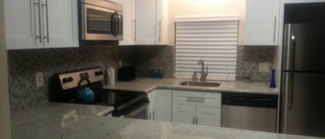 A kitchen with white cabinets, a stainless steel refrigerator, a microwave, a stove, and a sink.