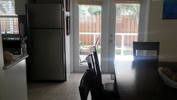 A kitchen with a refrigerator, a dining table with chairs, and a sliding glass door leading to a patio area.
