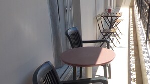 Un balcon avec une table ronde et deux chaises, une petite table avec une boisson, et une balustrade décorative.