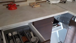 Une cuisine avec un tiroir contenant des ustensiles, une bouilloire rouge et un torchon plié.