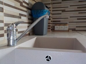 A modern kitchen sink with a chrome faucet, a trash bin, and a coffee maker on the counter.