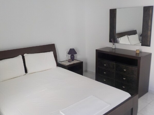 A bedroom with a large bed, a nightstand with a lamp, a dresser, and a mirror on the wall.