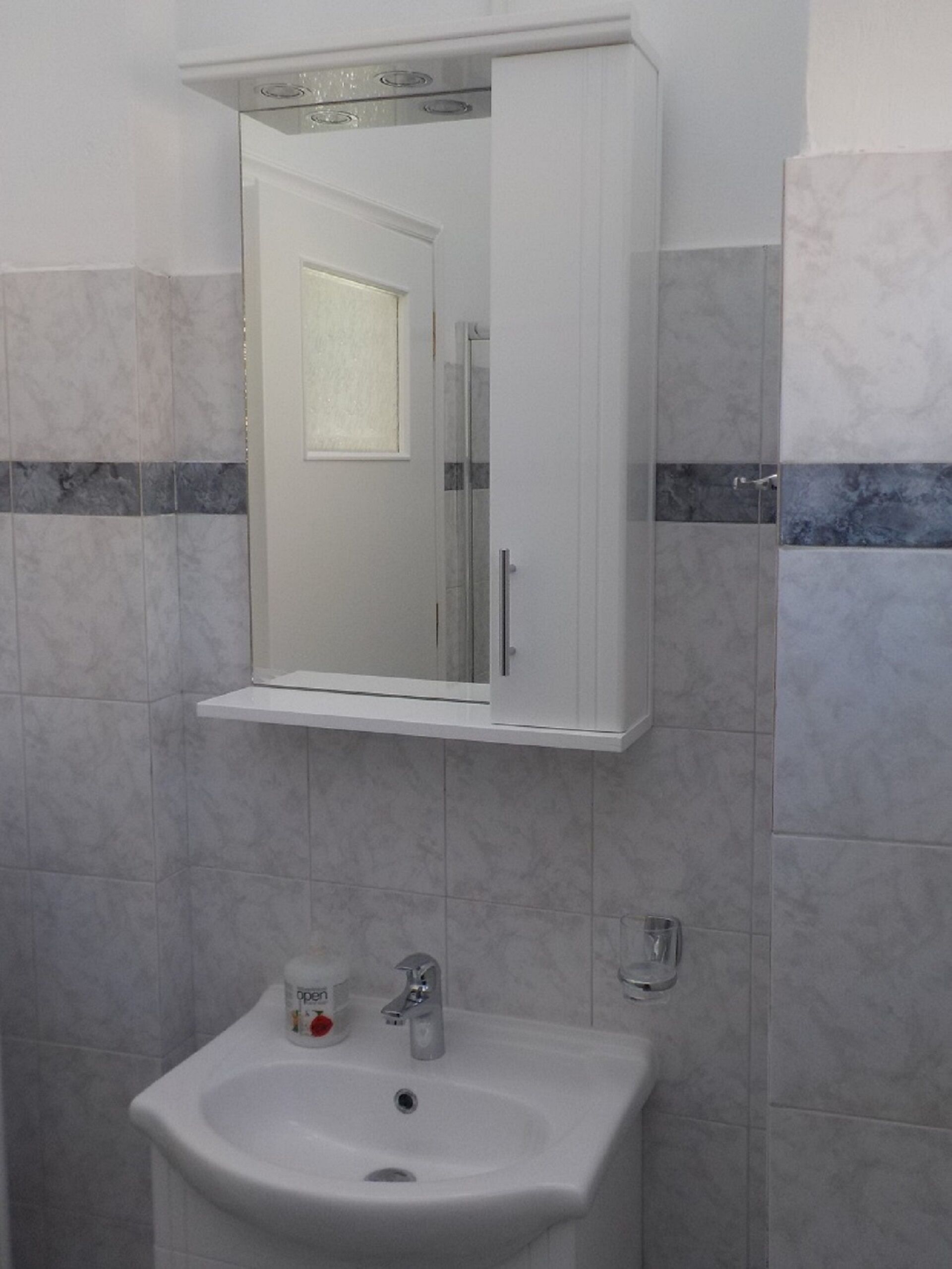 Une salle de bain avec un lavabo blanc, un miroir au-dessus, et un espace douche visible dans le reflet.