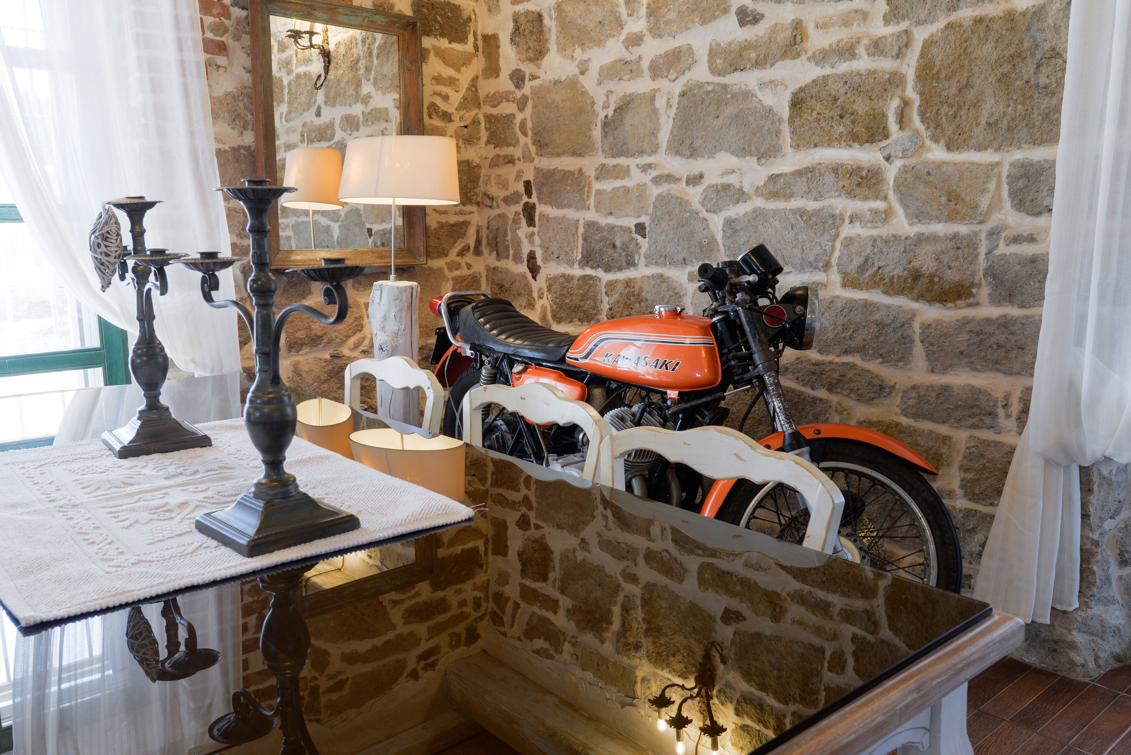 A stone wall, a motorcycle, a table with a lamp, and a candelabra.