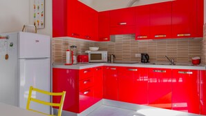 A modern kitchen with red cabinets, a white refrigerator, and a yellow chair.