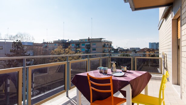 A balcony with a table set for two, a chair, and a view of the cityscape.
