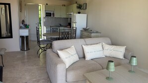 Ein Wohnzimmer mit einer Couch, zwei Lampen und einem Tisch. Im Hintergrund ist eine Küche mit Schränken und einer Mikrowelle zu sehen.