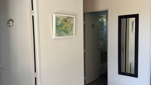 Ein Flur mit einer weißen Tür, einem Heizkörper, einer gerahmten Karte, einer Bank und einem Spiegel an der Wand.