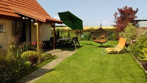 A well-maintained garden with a patio area, a hanging chair, and a lawn chair. - Cottage in Masuria. Mazury famous for its 2,000 lakes. (Gizycko)