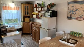 A compact kitchen with wooden cabinets, a refrigerator, and a microwave. There is a dining table with a tray and a chair. - Cottage in Masuria. Mazury famous for its 2,000 lakes. (Gizycko)