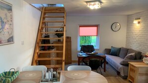 A cozy living room with a wooden dining table, a sofa, a ladder, and a window with a view of greenery. - Cottage in Masuria. Mazury famous for its 2,000 lakes. (Gizycko)