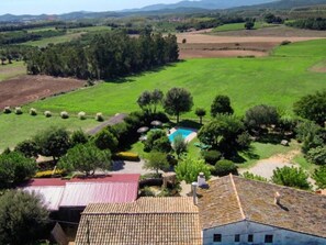 A residential property with a swimming pool, surrounded by green fields and trees.