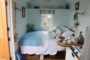 A cozy bedroom with a bed, a window, a dresser, and a small kitchen area. - shepard hut in the heart off somerset (nr wellssomerset)