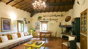 A cozy living room with a wooden ceiling, a sofa, a dining table, and a fireplace. - 3 bedroom house, private pool, gym, mature garden, walk to pizzeria, great views (Cardoso)
