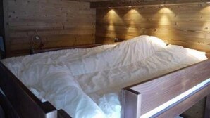 A wooden cabin bedroom with a bed covered in white bedding, wooden walls, and a sloped ceiling.