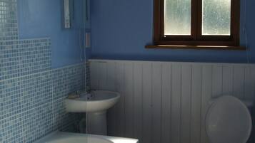 Een bad/douchecombinatie, handdoeken, zeep, toiletpapier