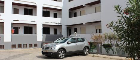 Un SUV plateado estacionado en un estacionamiento, con un edificio de varios pisos al fondo.