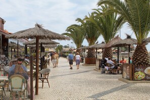 A cobblestone street lined with thatched umbrellas and palm trees, with people walking and dining at outdoor tables. - Seaview apartment Alvor (Alvor)