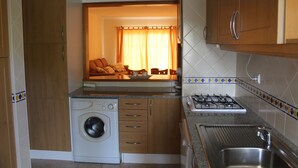 Una cocina compacta con lavadora, estufa a gas y armarios de madera.