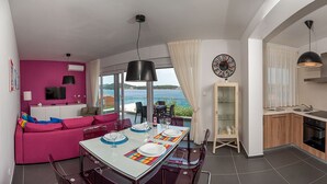 A modern apartment with a balcony, a dining area, a kitchen, and a living room with a pink sofa.