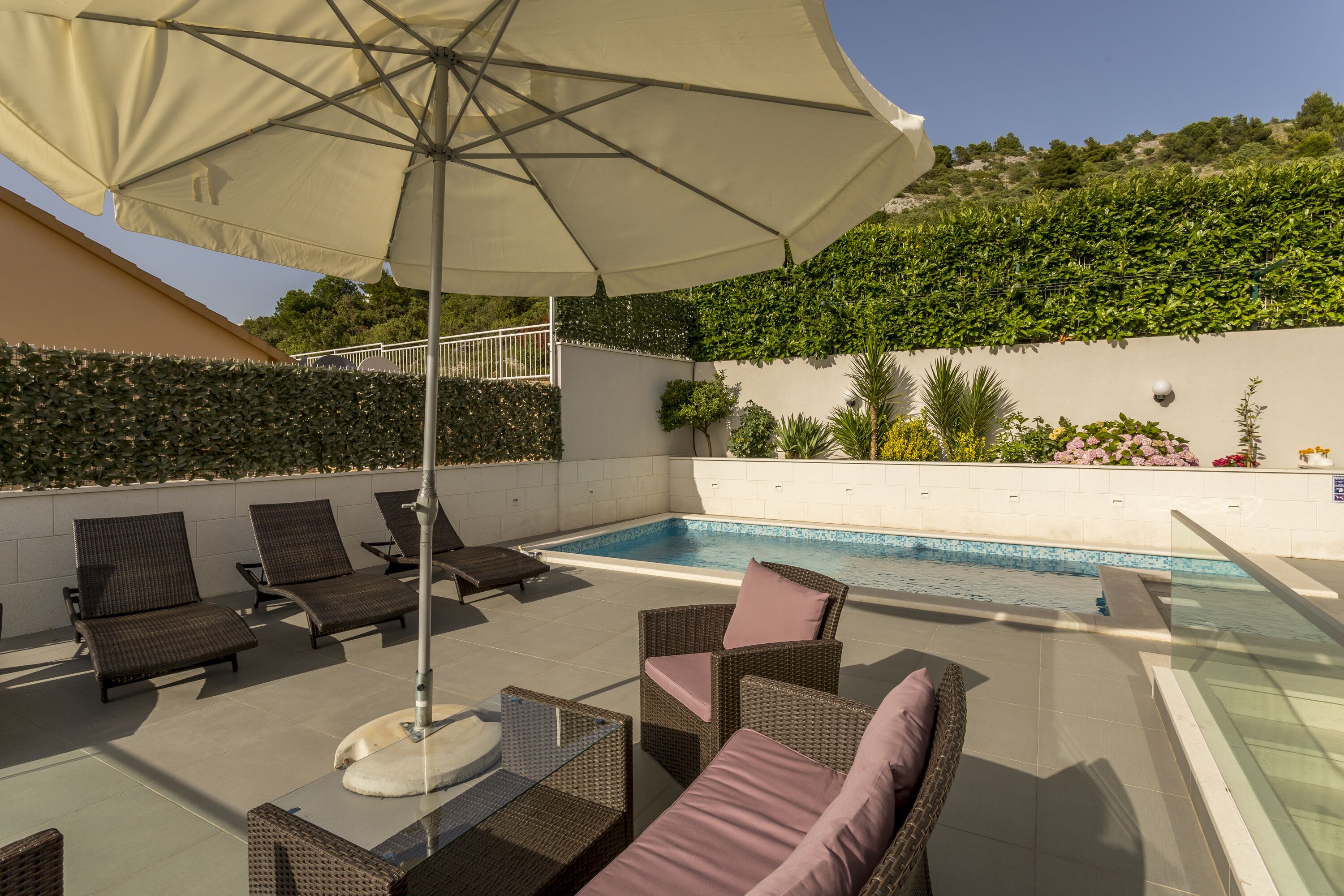 Area piscina sul tetto con poltrone prendisole, un ombrellone grande e una piscina coperta da vetri.