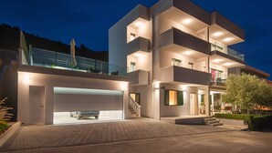 A modern multi-story building with a garage, outdoor seating, and a staircase leading to the entrance.