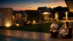 A poolside area with outdoor seating, a stone wall, and a well-lit patio.