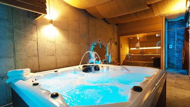 A hot tub with a wooden interior, a towel on the side, and a shower area visible through the doorway.