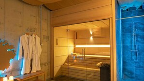 A modern bathroom with a glass shower enclosure, a wooden bench, and a towel rack with robes.