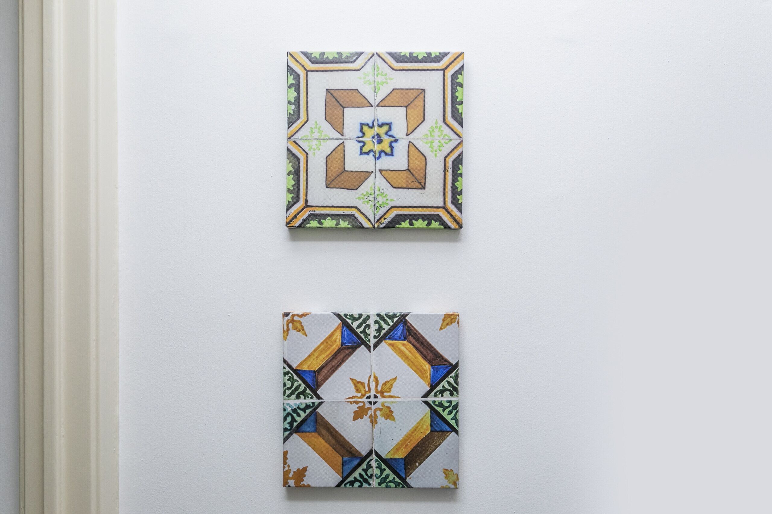 Zwei quadratische Fliesen mit geometrischen Mustern an einer Wand.