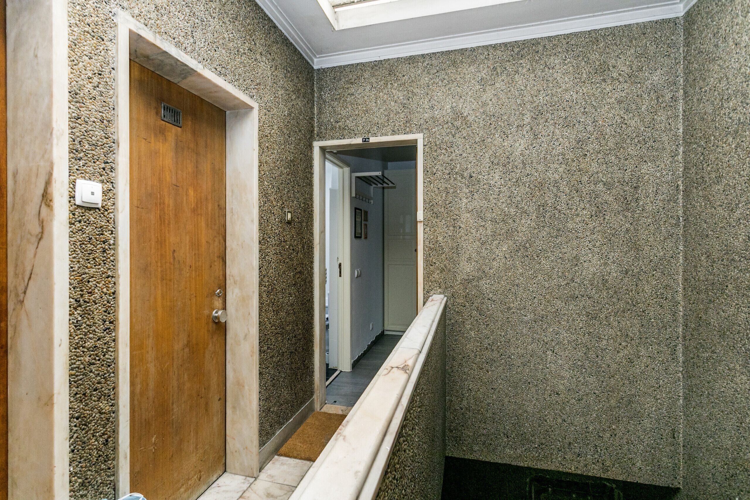 A narrow hallway with textured walls, a wooden door, and a white railing.